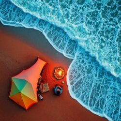 Overhead bird’s eye view, warm terracotta and cool teal colors. Chabahar beach camping scene at sunset. Colorful tent, waves, campfire, person. Earthy and cool color contrast, top-down perspective